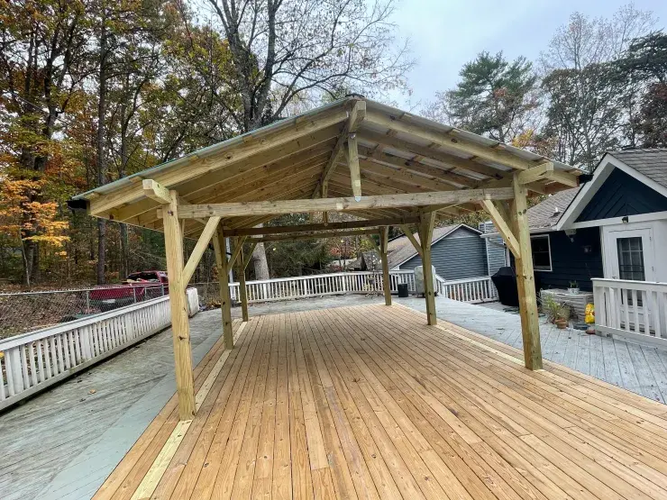 A newly framed pavilion with exposed rafters standing over a fresh pressure-treated deck in the mountains.