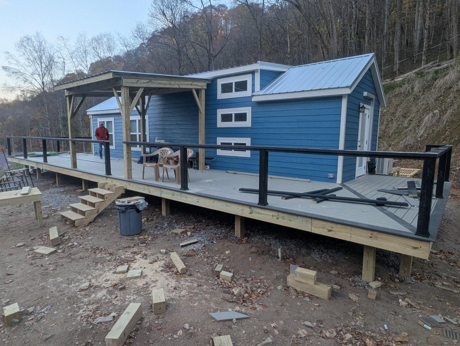 A wrap-around deck on a blue mountain house, finished with black railing and a covered porch.