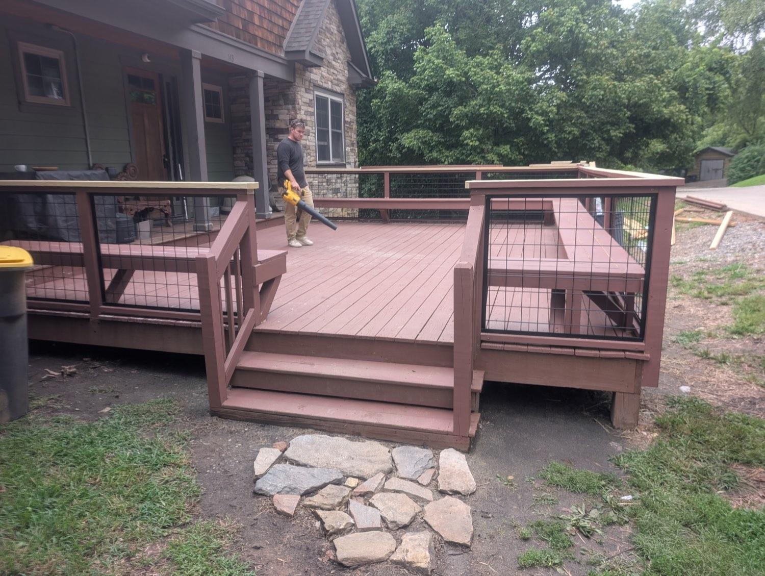 The finished deck with black wire-mesh railing, new steps and a stone landing down to the grass.