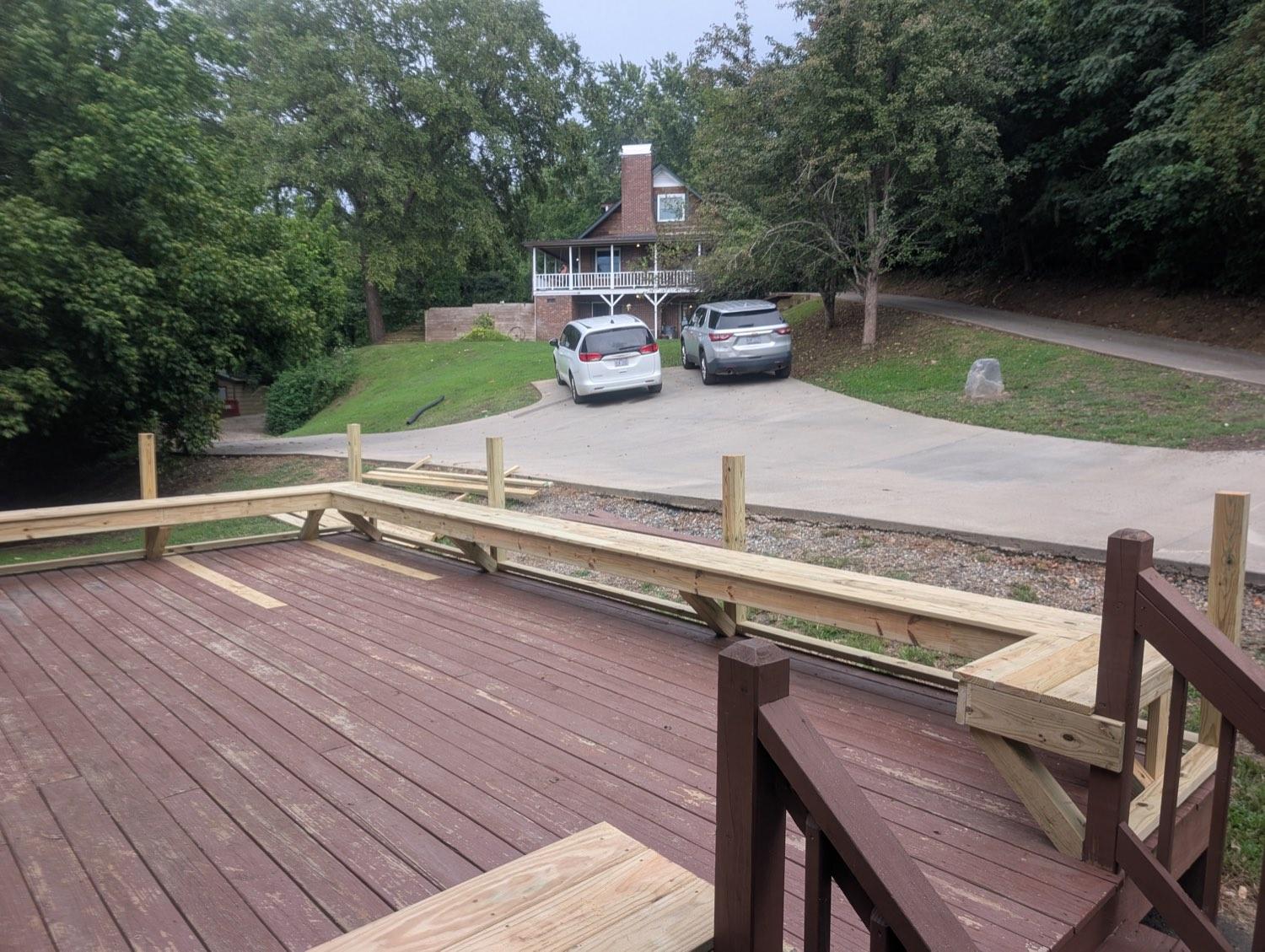 A maroon deck with the new pressure-treated railing frame being fitted, looking out across the drive.