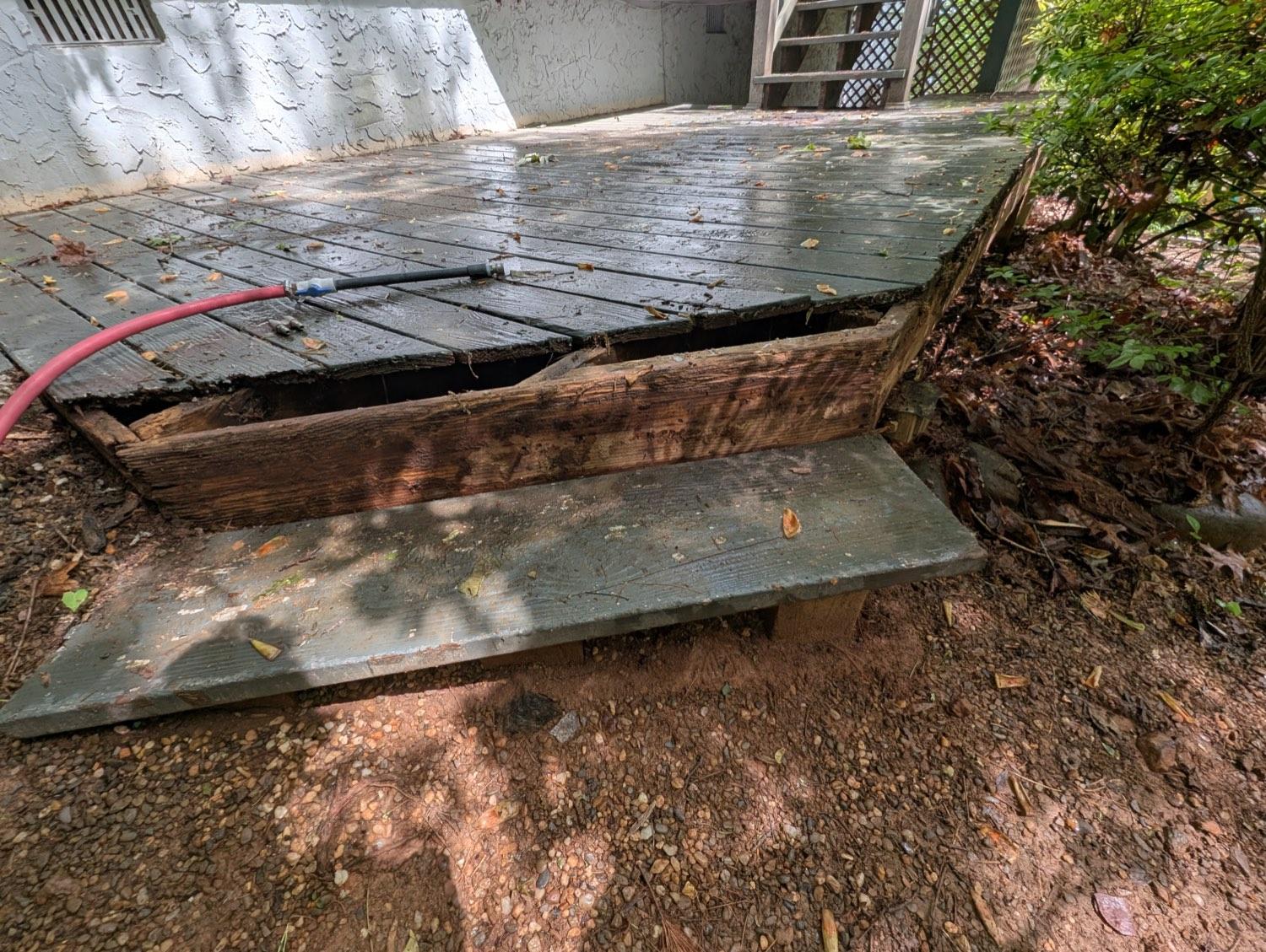 A collapsed section of deck boards exposing a rotted, blackened rim joist underneath.