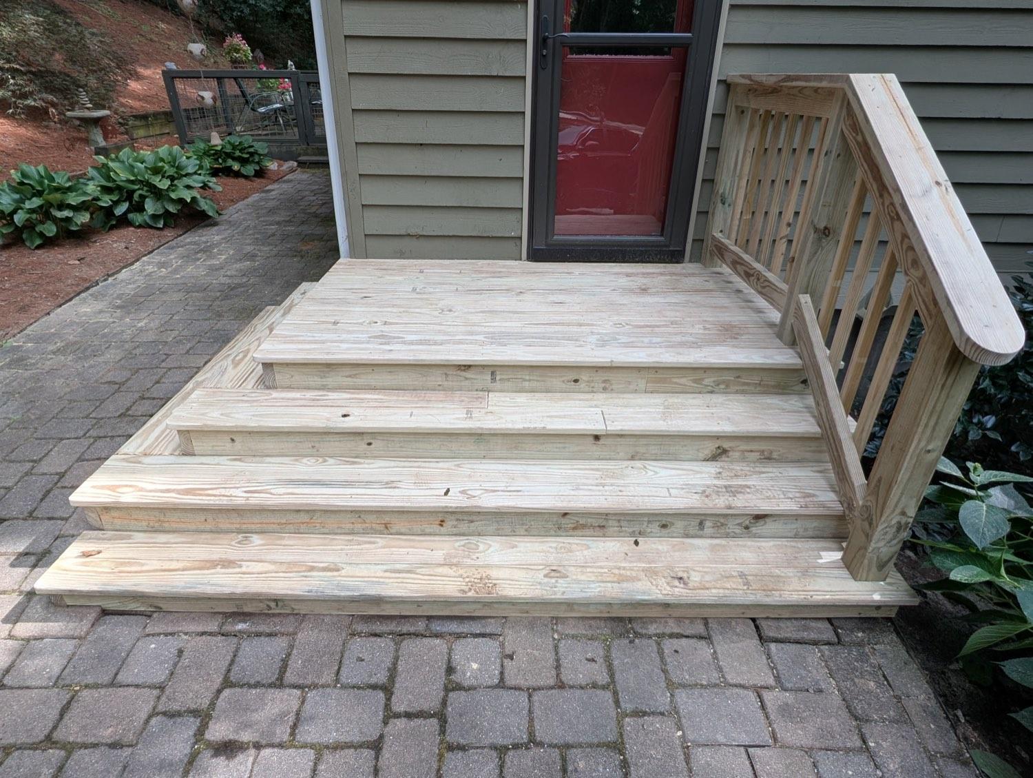 New wide pressure-treated steps at the same back door, with a pine handrail down to the patio.