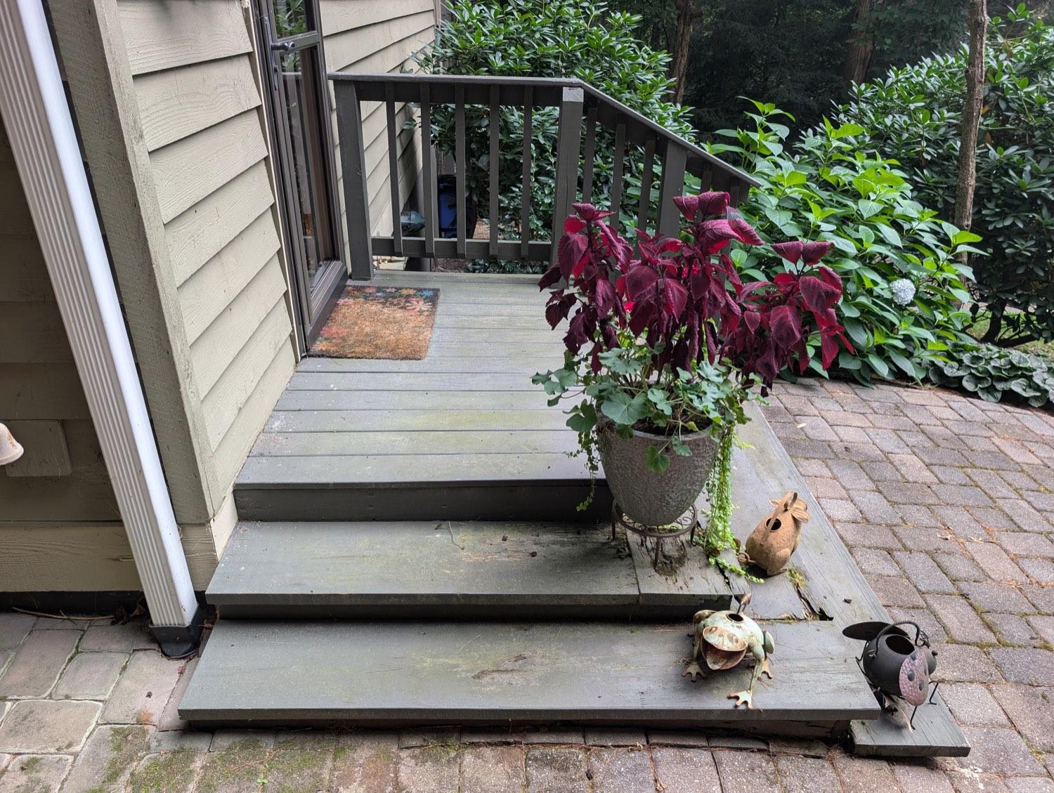 Weathered green-grey back steps, mossy and pulling away from the house above a brick patio.