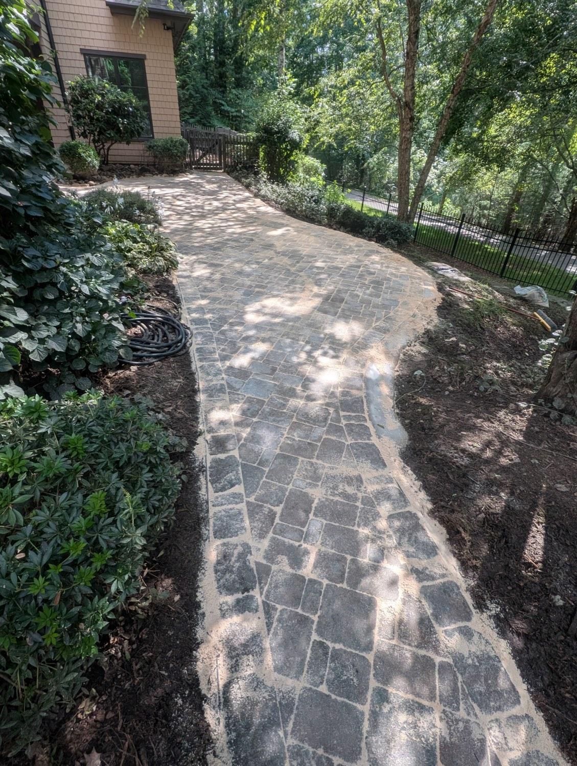 The finished cobblestone walkway curving along the side of the house, edged tight against the planting beds.