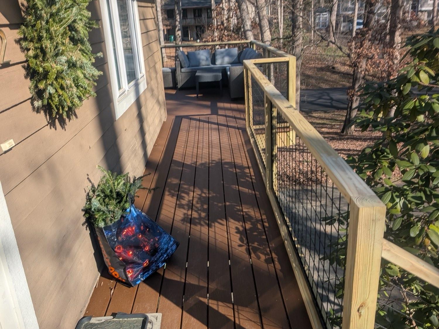 A composite deck running along the side of a house with a pressure-treated wire-mesh rail and a seating area at the end.